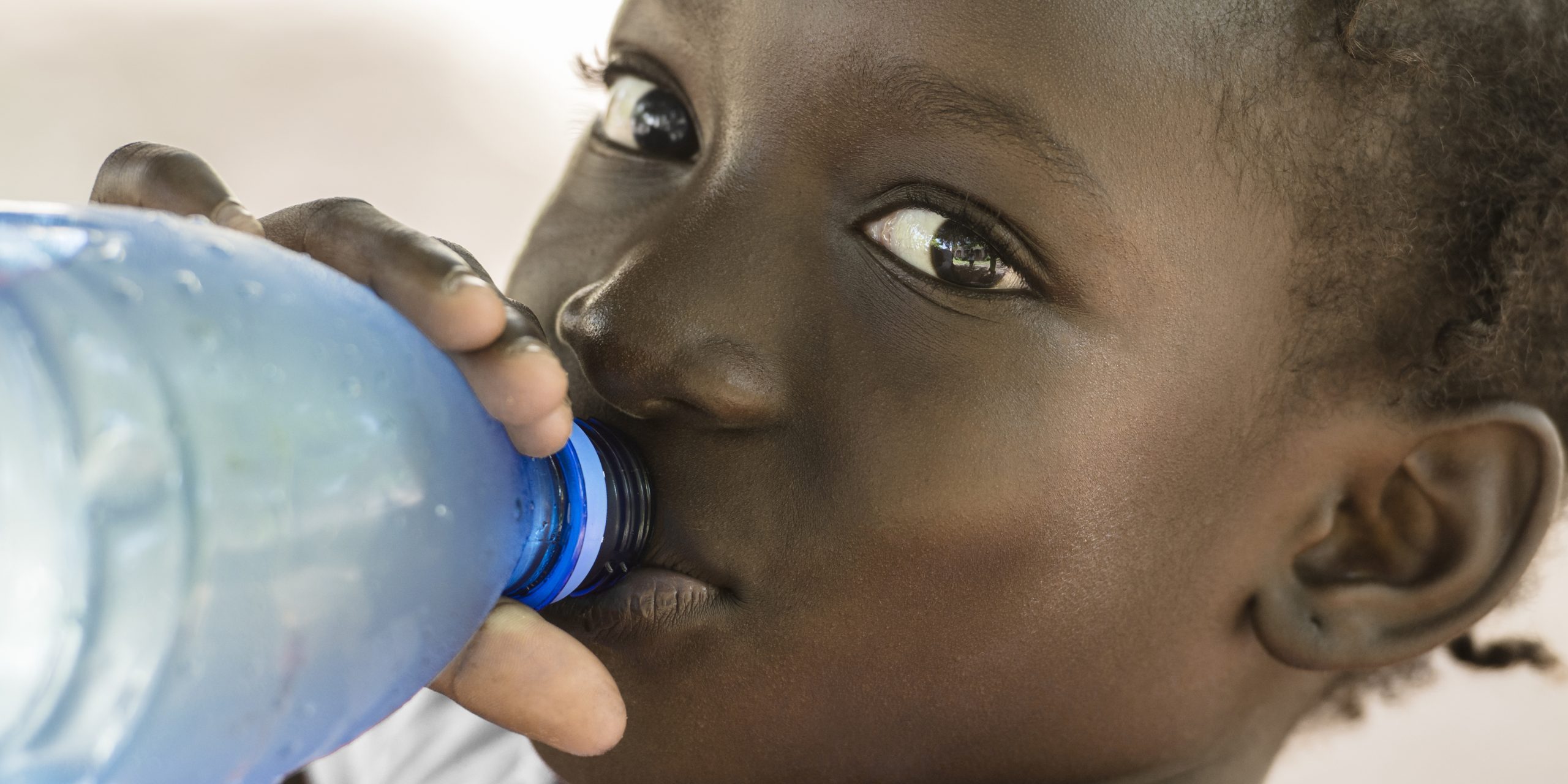 Poverty Symbol in Mali: African Black Girl Drinking Heathy Fresh Water from a bottle.